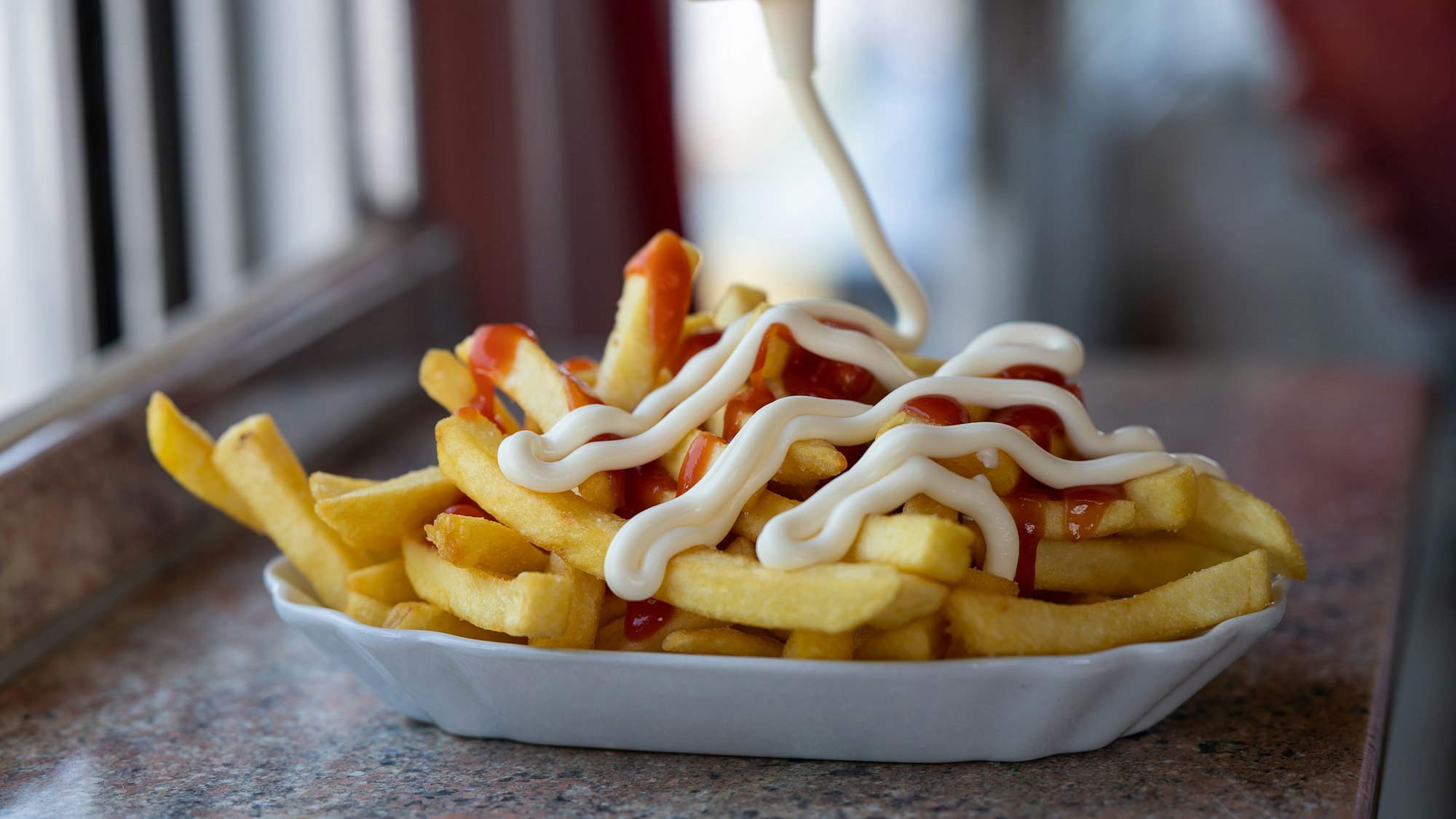 Pommes mit Ketchup und Mayo stehen auf einem Tisch.
