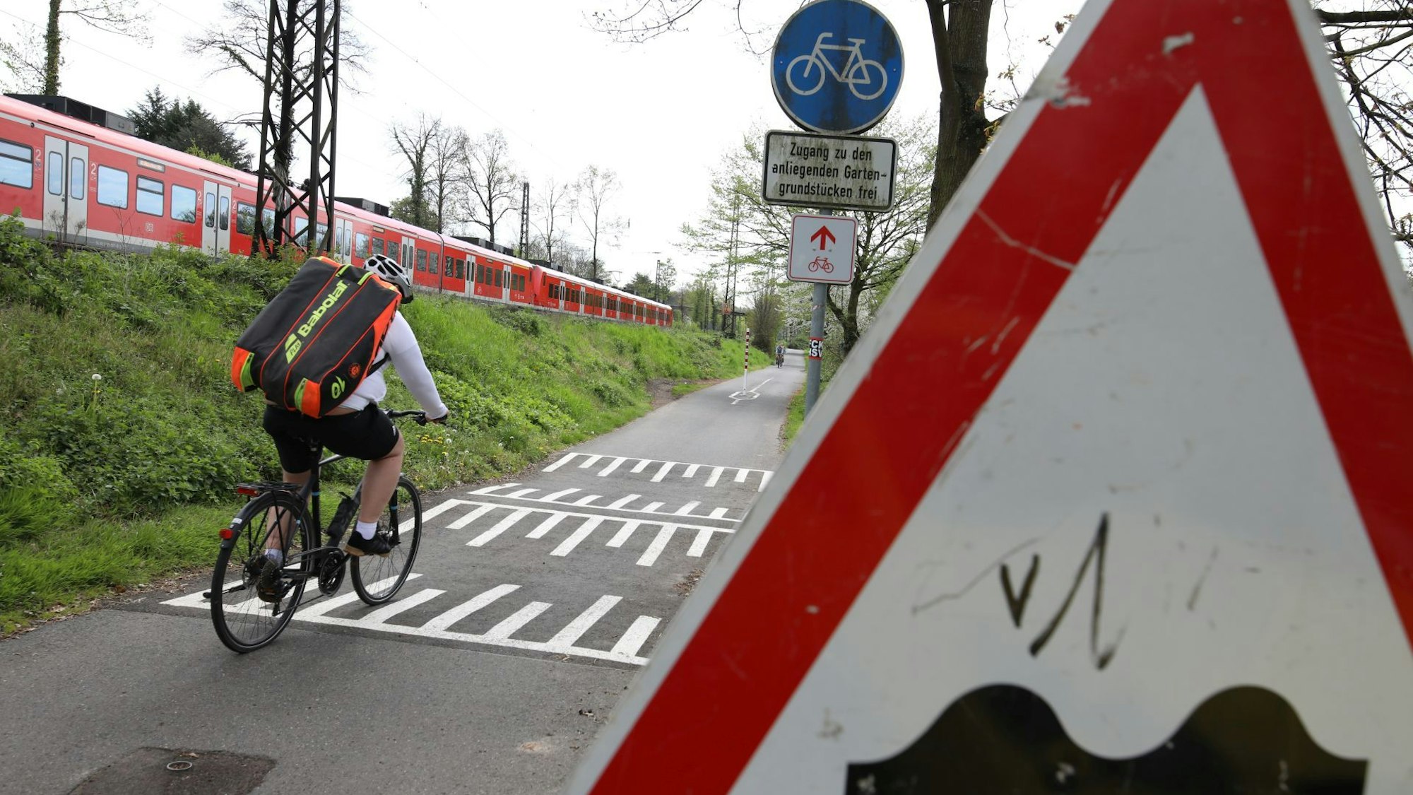 Ein Radfahrer fährt über markierte Bodenwellen auf dem Rheinradweg in Rhöndorf, ein Straßenschild weist auf die Unebenheiten hin.