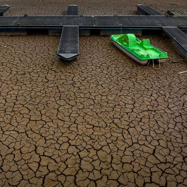 Die Stege einer Anlegestelle im Sau-Stausee in Spanien liegen komplett im Trockenen. Der Boden hat überall Risse. Ein neongrünes Tretboot liegt neben einem Anleger auf dem trockenen Boden.