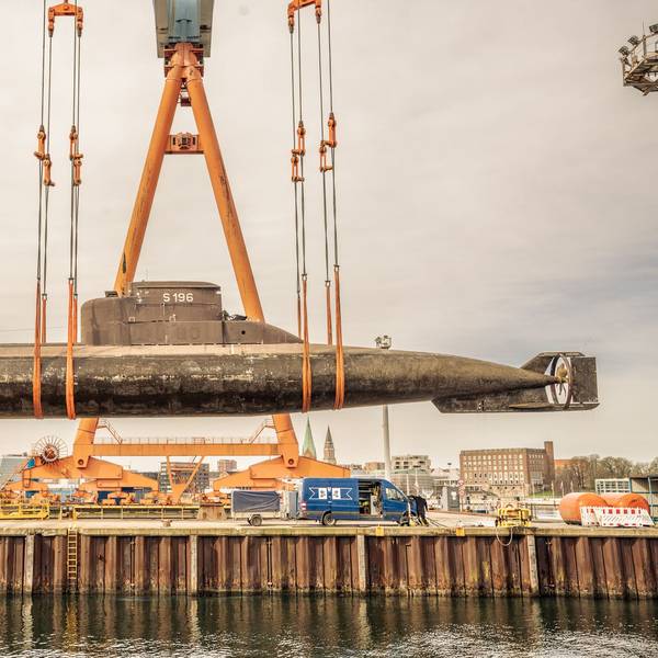 Ein großes U-Boot hängt in Schlingen an einem großen Kran und hängt über einem Seedock.