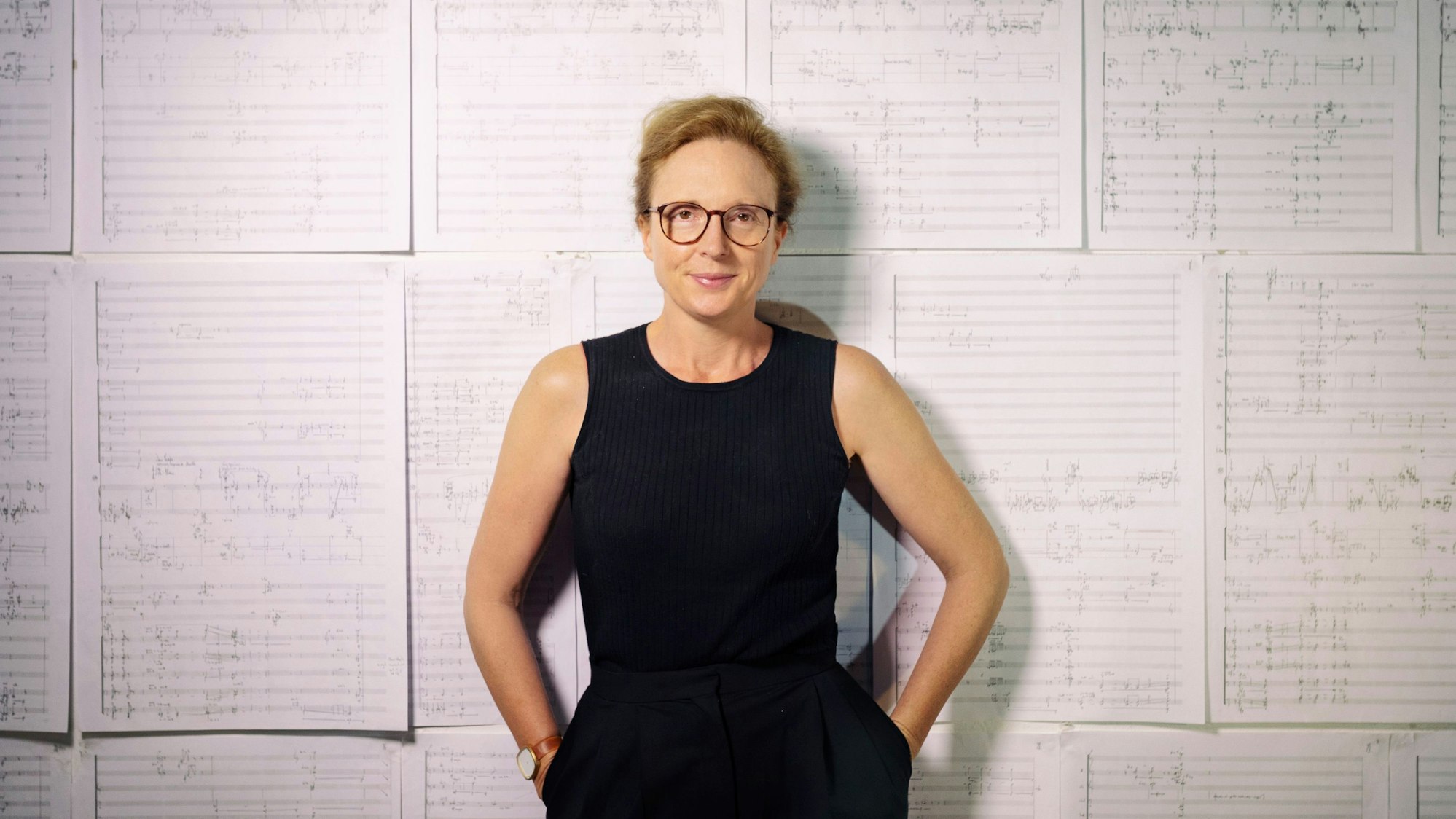 Die Britische Komponistin Rebecca Saunders. Sie steht vor einer Wand, in der große Zettel mit Noten hängen.