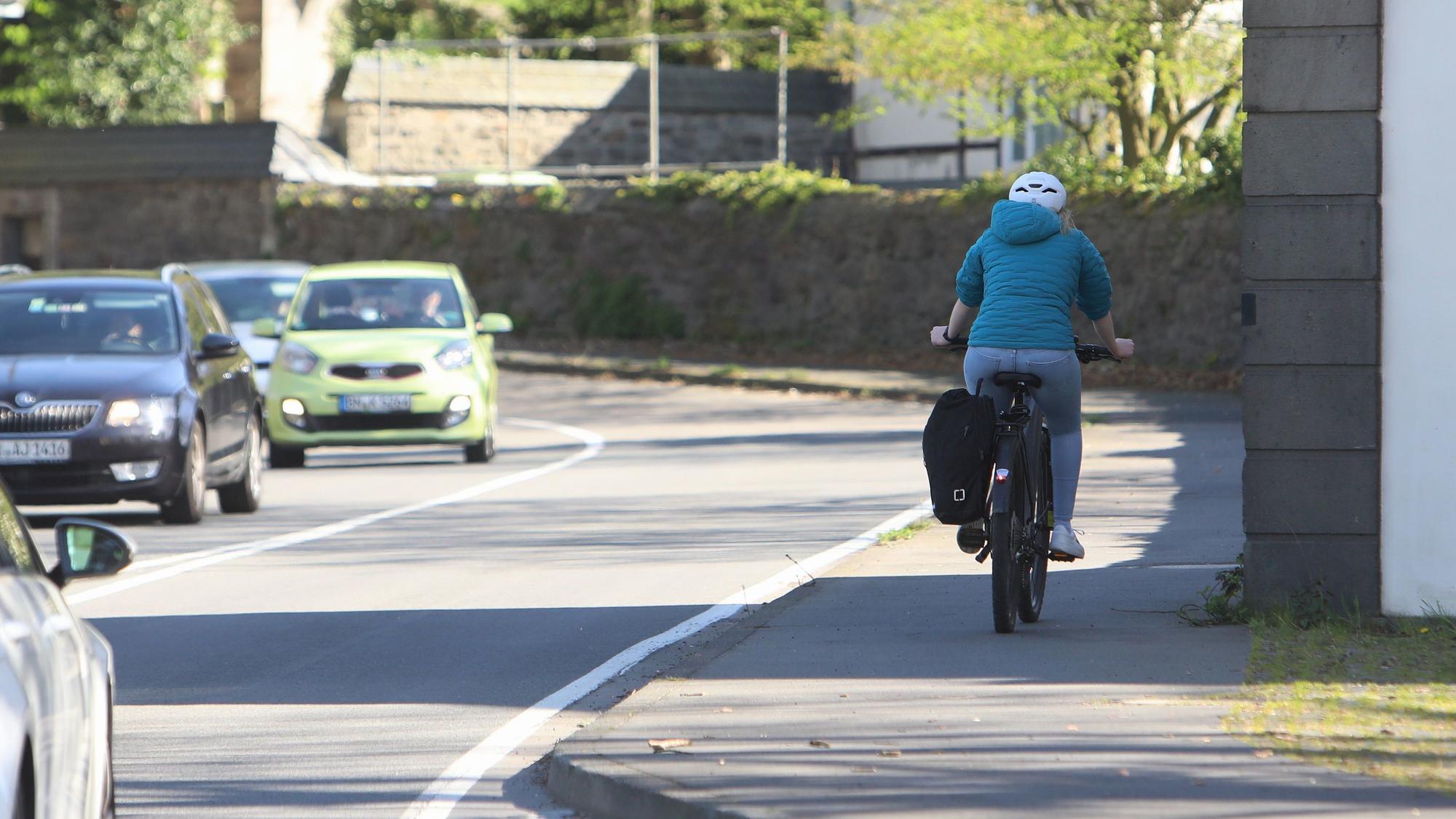 Eine Radfahrerin fährt auf dem relativ schmalen Fuß-Radweg entlang der stark befahrenen Landesstraße 268 in Höhe des Klosters Heisterbach.