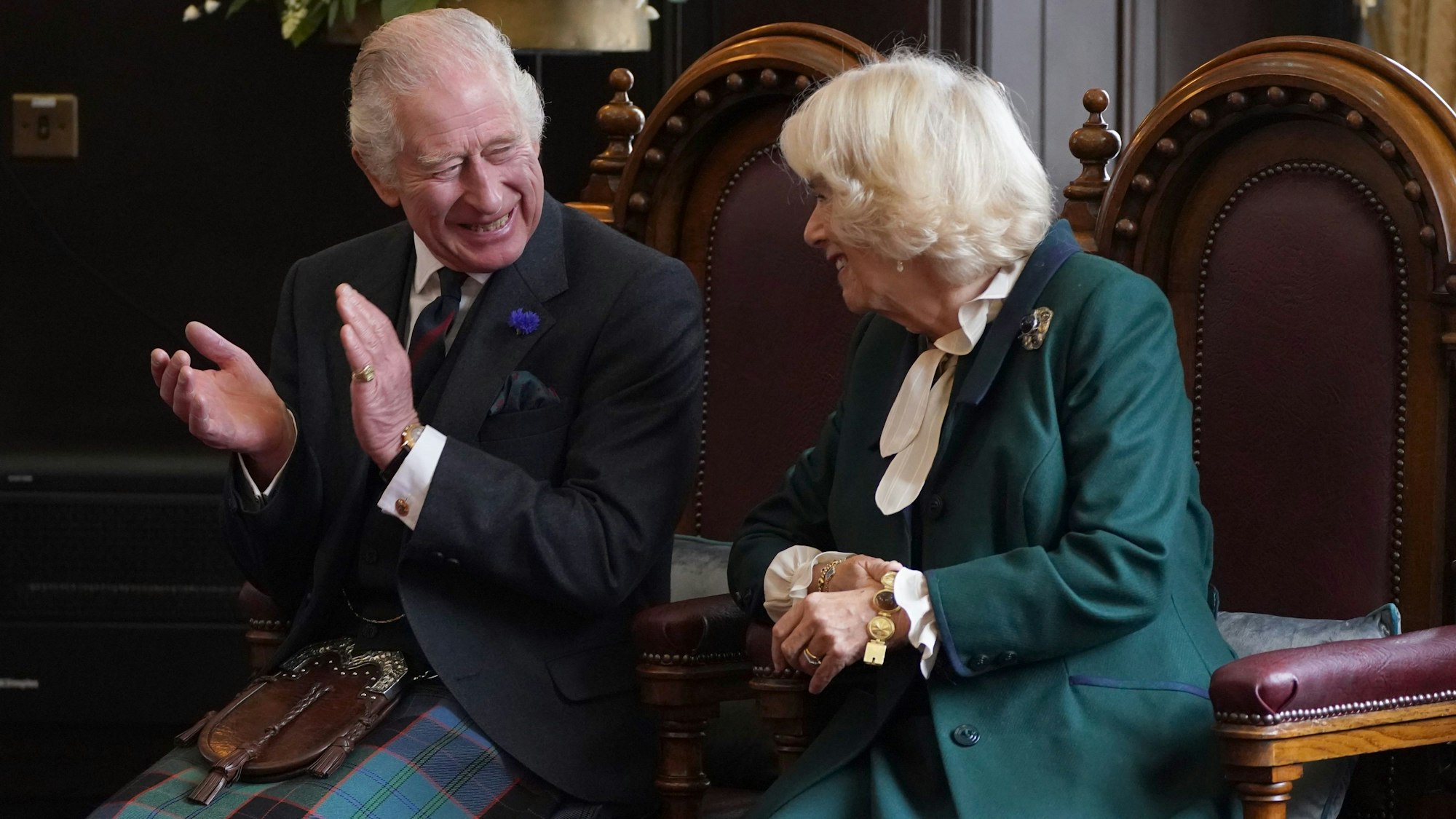 Charles III. und seine Camilla sitzen auf Sesseln und freuen sich. Charles klatscht in die Hände.