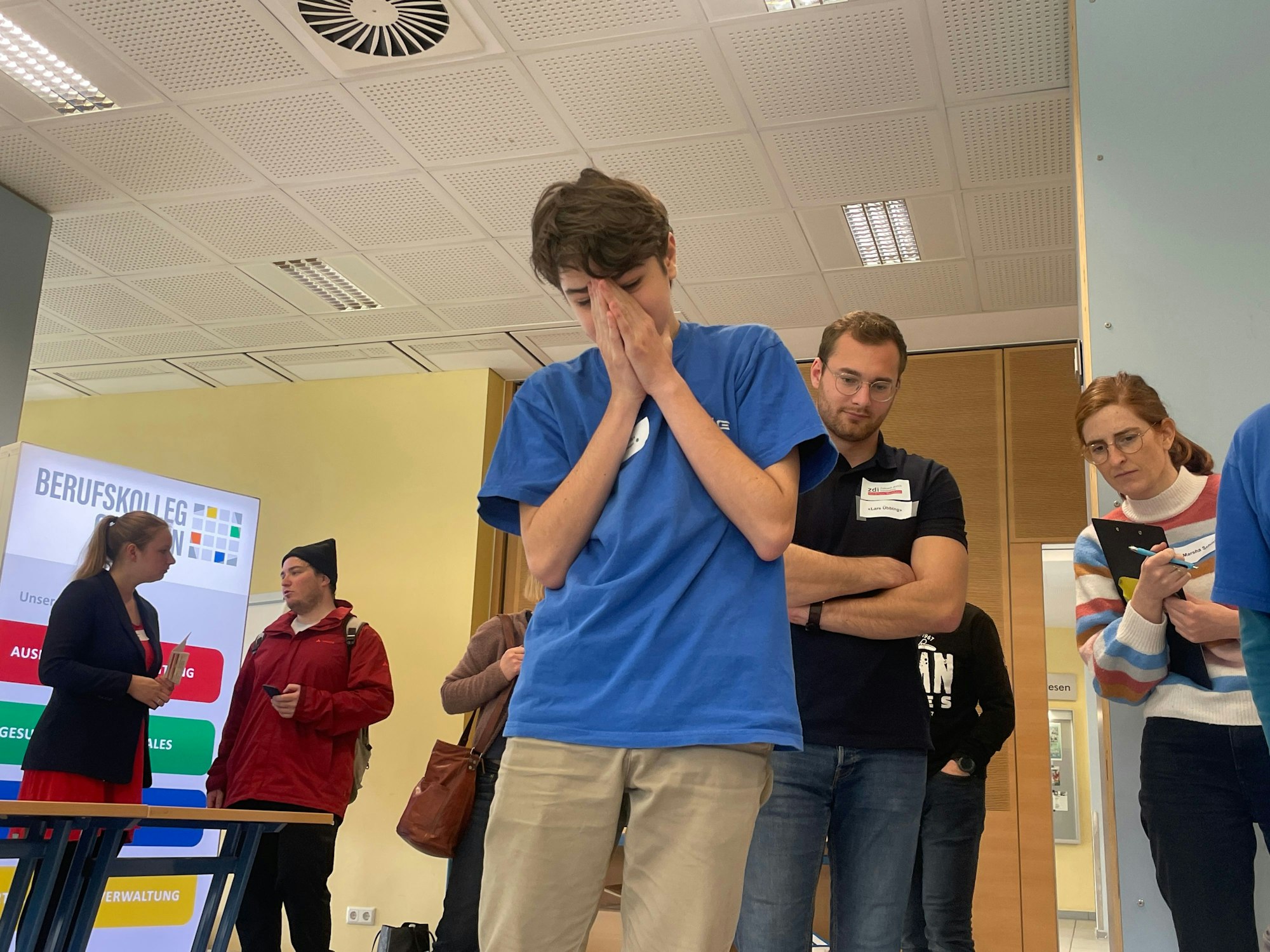Enttäuschter Schüler blickt auf das Spielfeld. Schiedsrichter beobachten von hinten.
