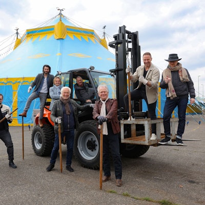 Männer auf und vor einem Traktor, der vor einem Zirkuszelt steht.