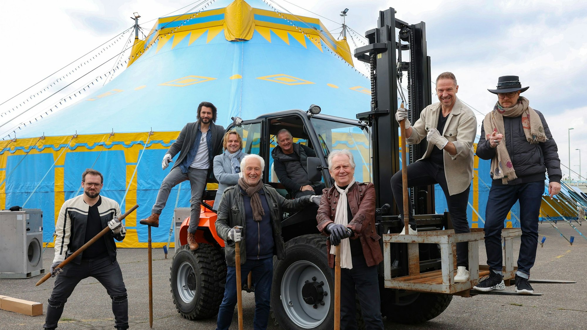 Männer auf und vor einem Traktor, der vor einem Zirkuszelt steht.
