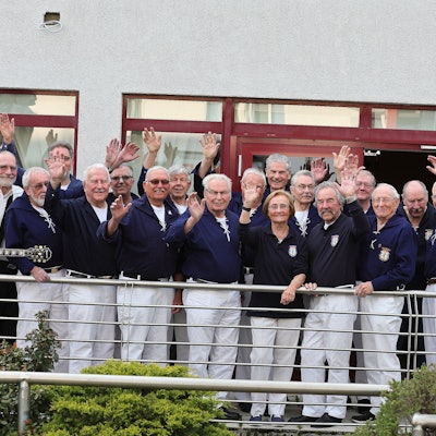 Der 1. Kölner Shanty-Chor steht winkend auf einer Terrasse, die einzige Dame auf dem Bild darf allerdings nicht mitsingen.