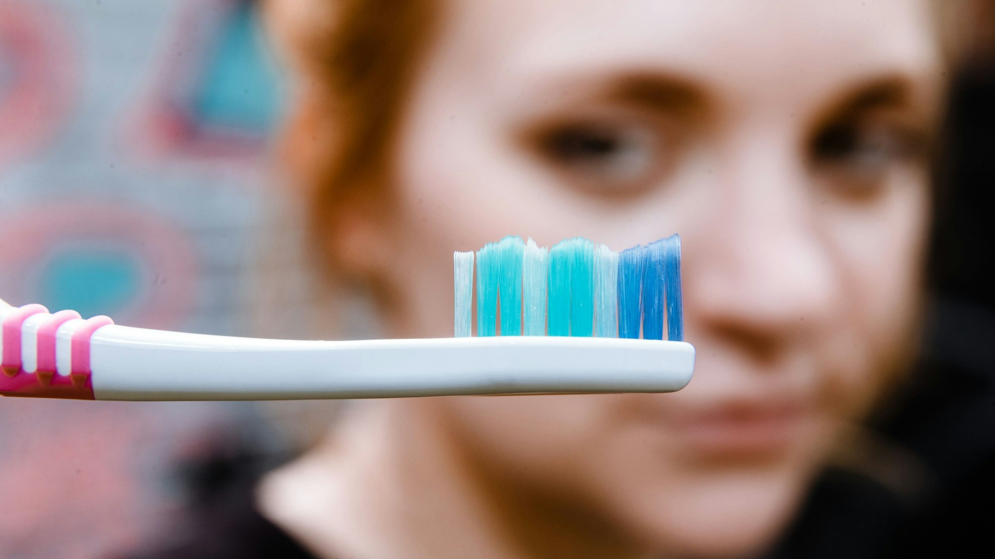 Das Gesicht einer Frau ist unscharf hinter einer Zahnbürste zu erkennen.