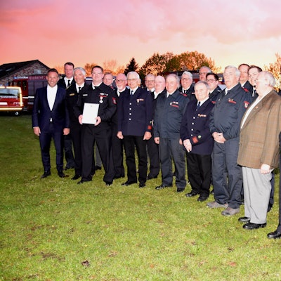 Die Personen stehen draußen auf einer Wiese, im Hintergrund ein Sonnenuntergangs-Himmel