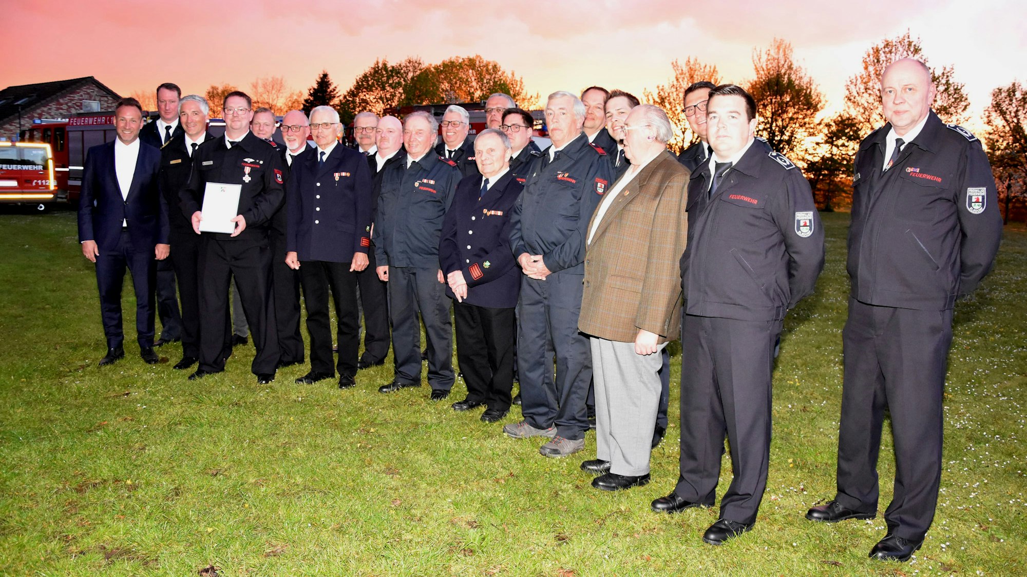 Die Personen stehen draußen auf einer Wiese, im Hintergrund ein Sonnenuntergangs-Himmel