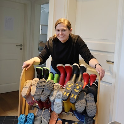 Die Auszubildende Agi Oskedra steht in einer Kita hinter einem Regal mit Kinder-Stiefeln.