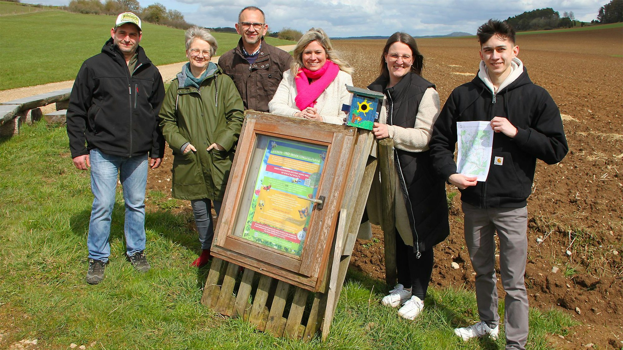 Sechs Personen stehen vor einem Acker, auf dem in den nächsten Monaten zahlreiche Blumen blühen werden.