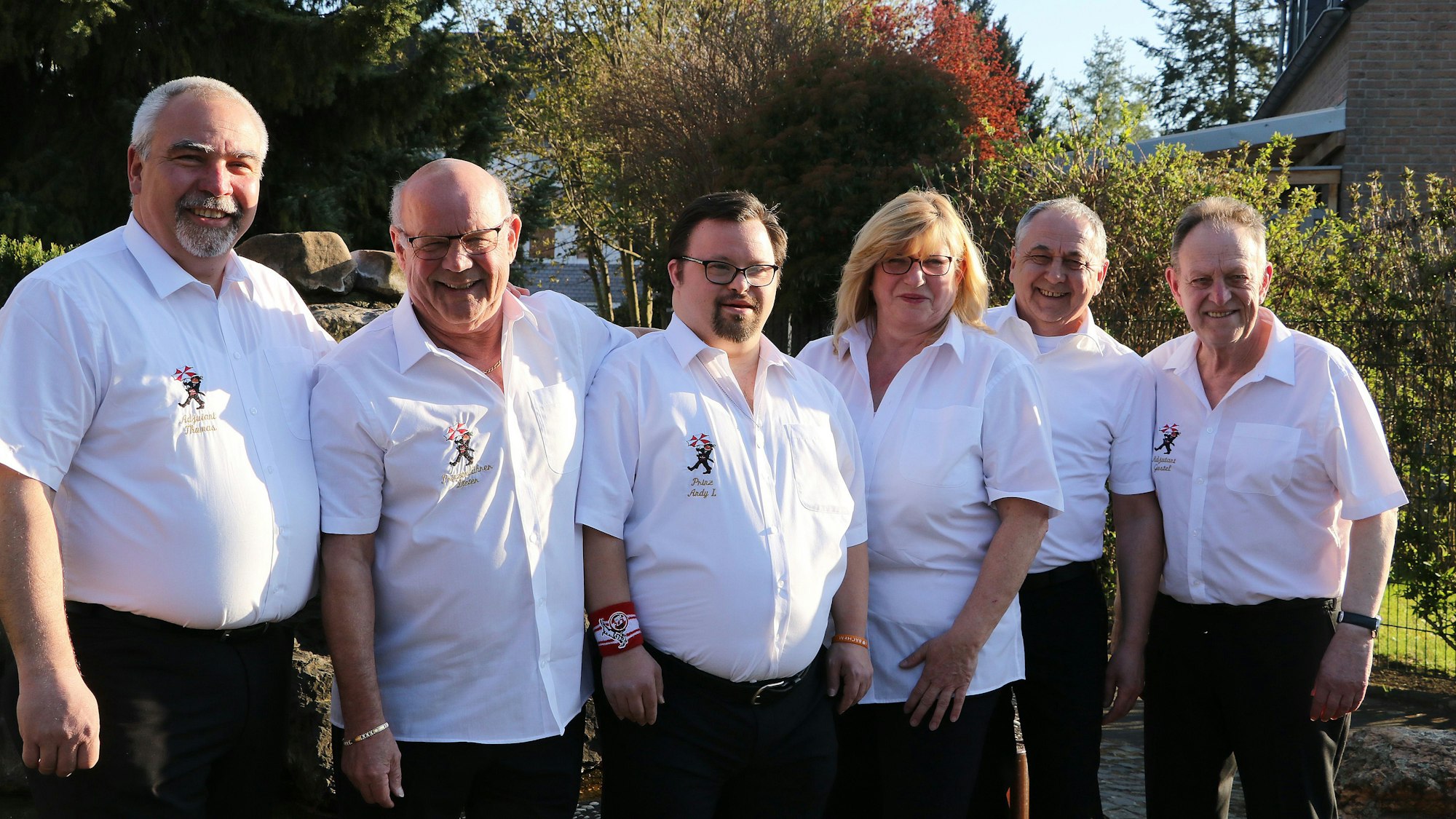 Die Personen tragen alle das weiße Hemd der Gesellschaft, sie stehen draußen.