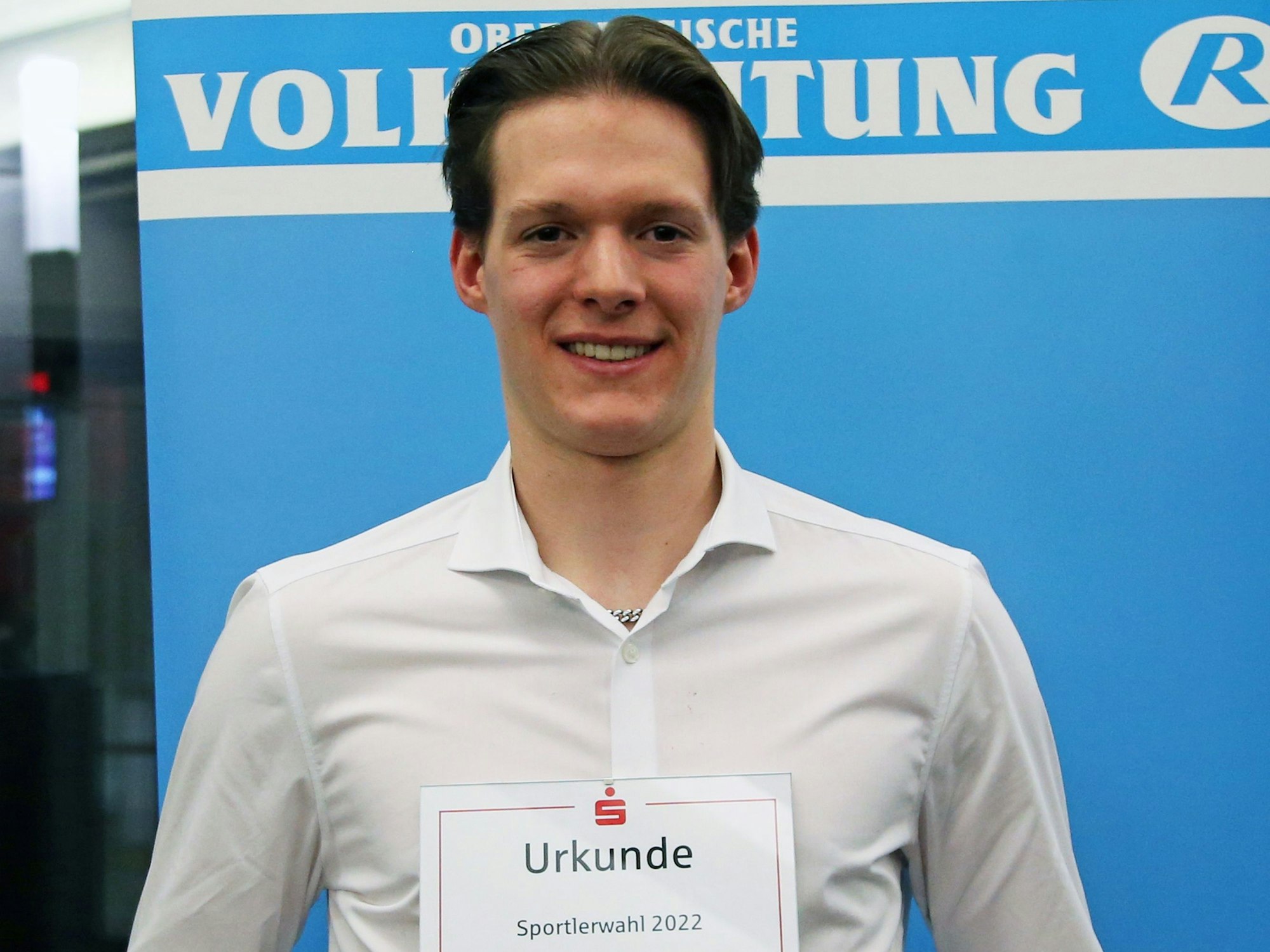 Zu sehen ist ein junger Mann, der eine Urkunde präsentiert.