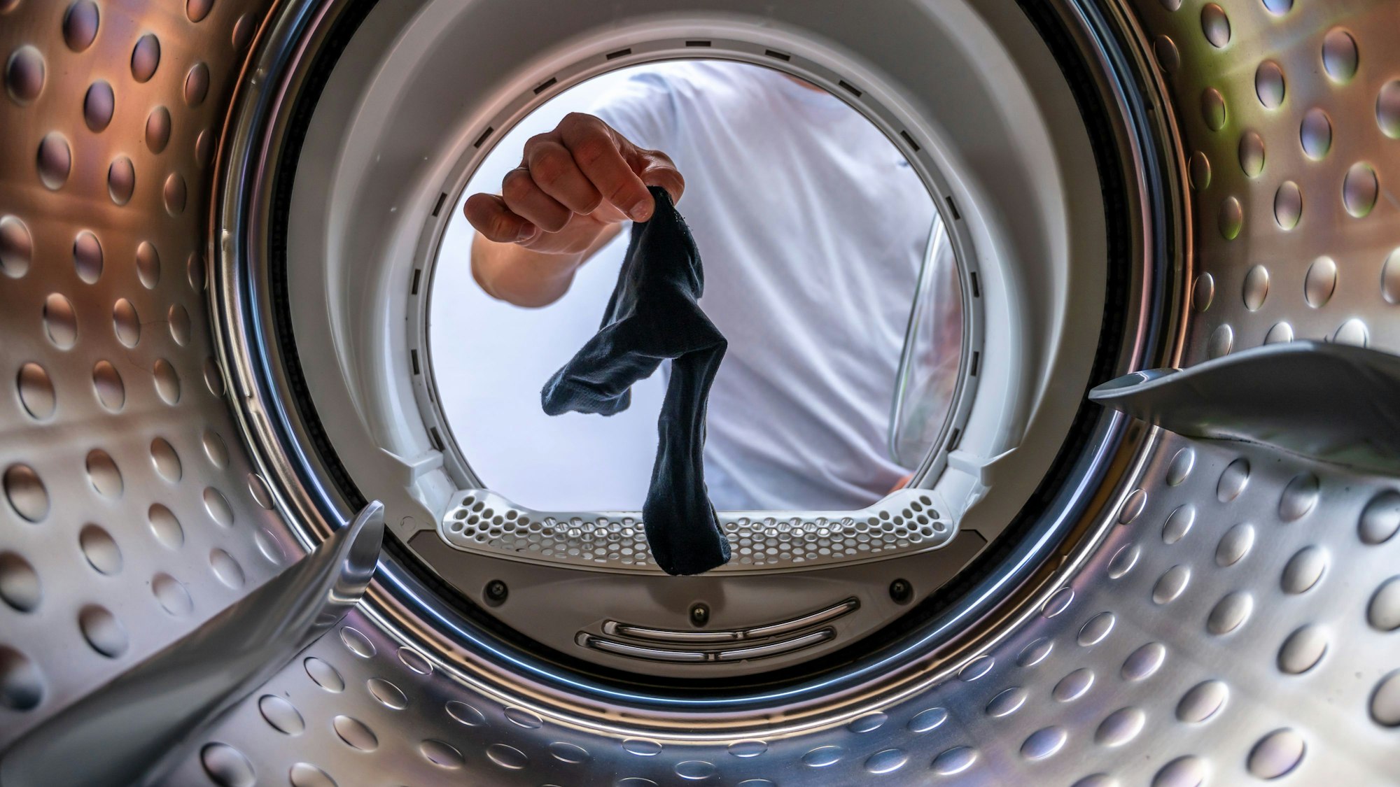 Blick in die Trommel einer Waschmaschine, ein Mann hält eine einzelne Socke ins Bild