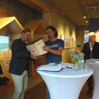 Landrat Markus Ramers überreicht Stefan Brings, dem Paten der Aktion „Zu Gast in der eigenen Heimat“ ein „Hummelhaus“. Um sie herum drei weitere Personen. Sie befinden sich drinnen.