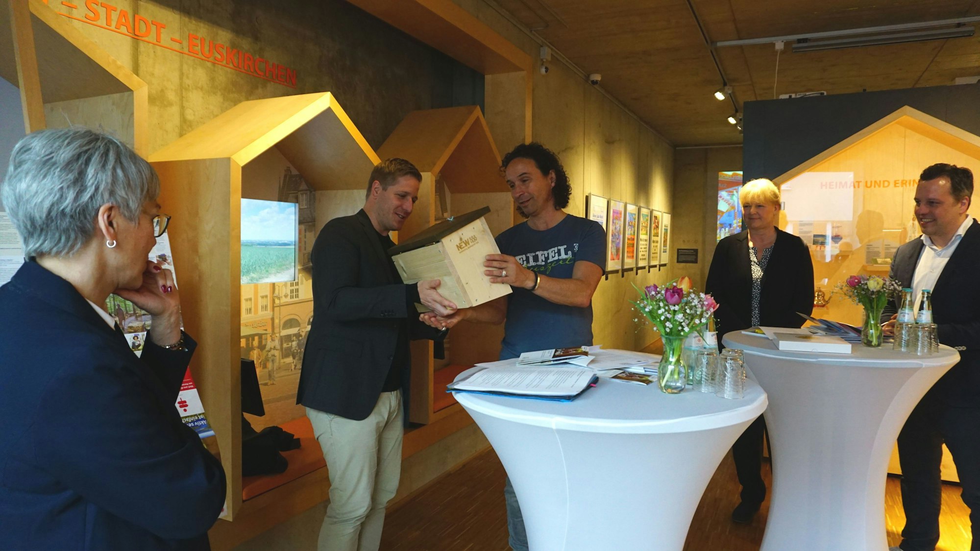 Landrat Markus Ramers überreicht Stefan Brings, dem Paten der Aktion „Zu Gast in der eigenen Heimat“ ein „Hummelhaus“. Um sie herum drei weitere Personen. Sie befinden sich drinnen.