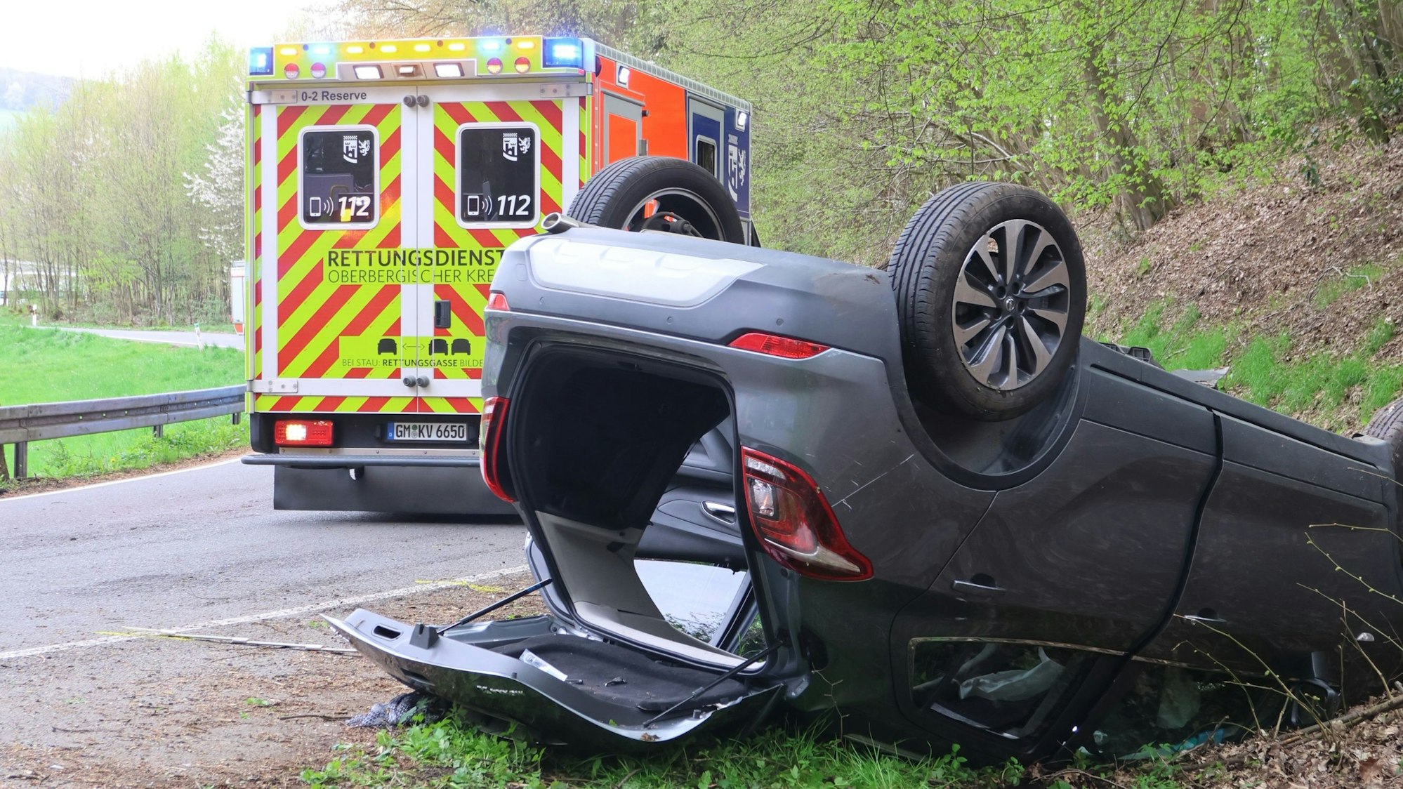 Ein Auto liegt mit geöffneter Heckklappe auf dem Dach. Im Hintergrund steht ein Rettungswagen.