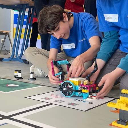 Schüler nimmt letzte Anpassungen am Roboter vor der entscheidenden Runde vor.
