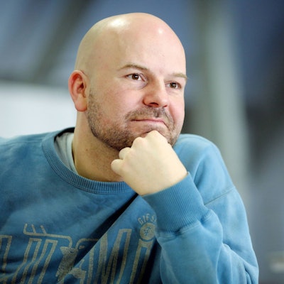 Manuel Moser stützt sich das Kinn mit der Hand. Er hat eine Glatze und einen 3-Tage-Bart. Er trägt einen blauen Pulli.