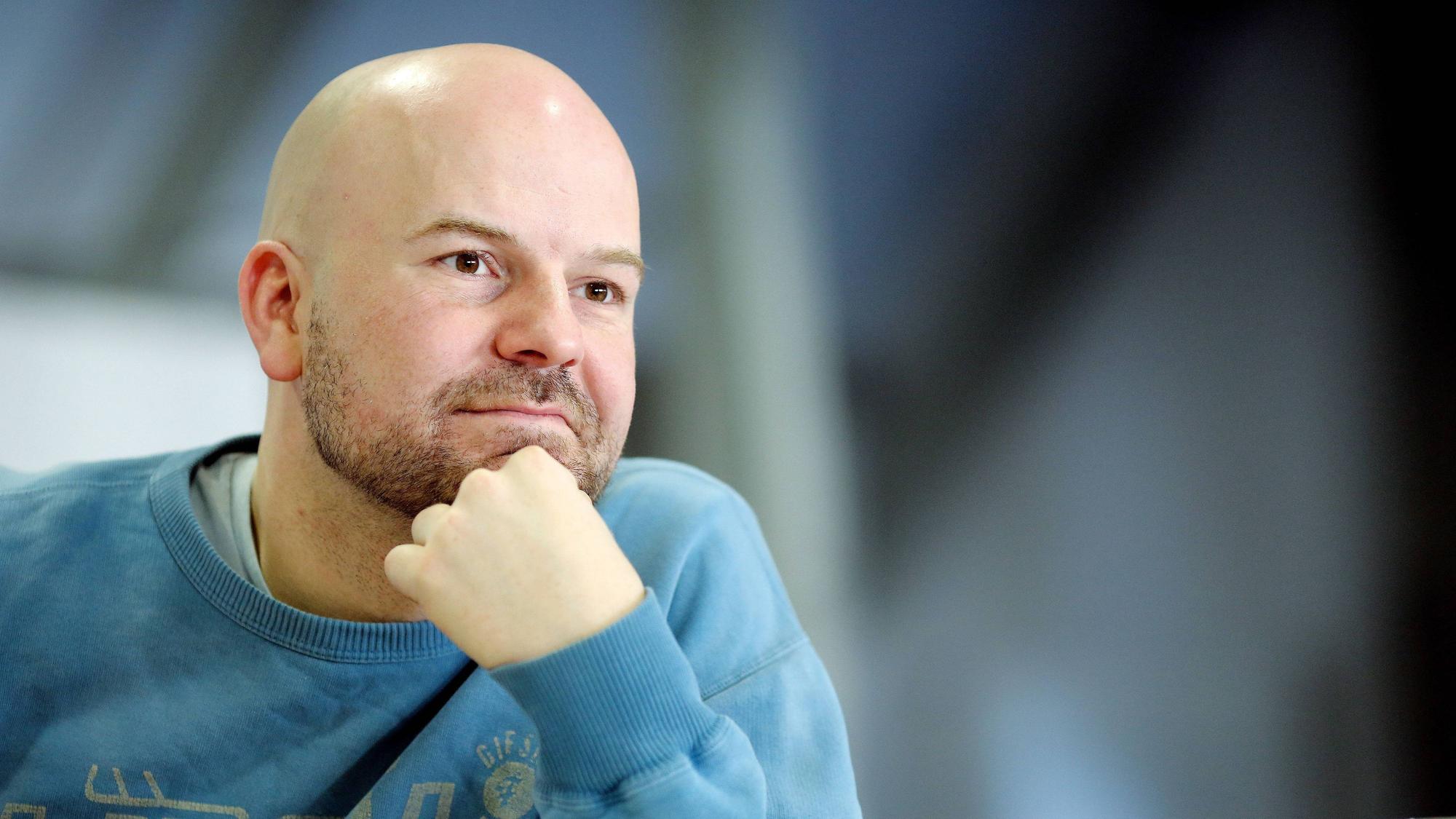 Manuel Moser stützt sich das Kinn mit der Hand. Er hat eine Glatze und einen 3-Tage-Bart. Er trägt einen blauen Pulli.