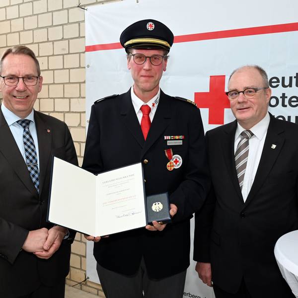 Sascha Habernickel steht in Uniform zwischen zwei Männern im Anzug und hält lächelnd seine Auszeichnung und Medaille in die Kamera.