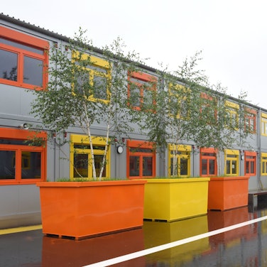Containerbauten mit orangen und gelben Fenstern und bunten Pflanzkübeln.