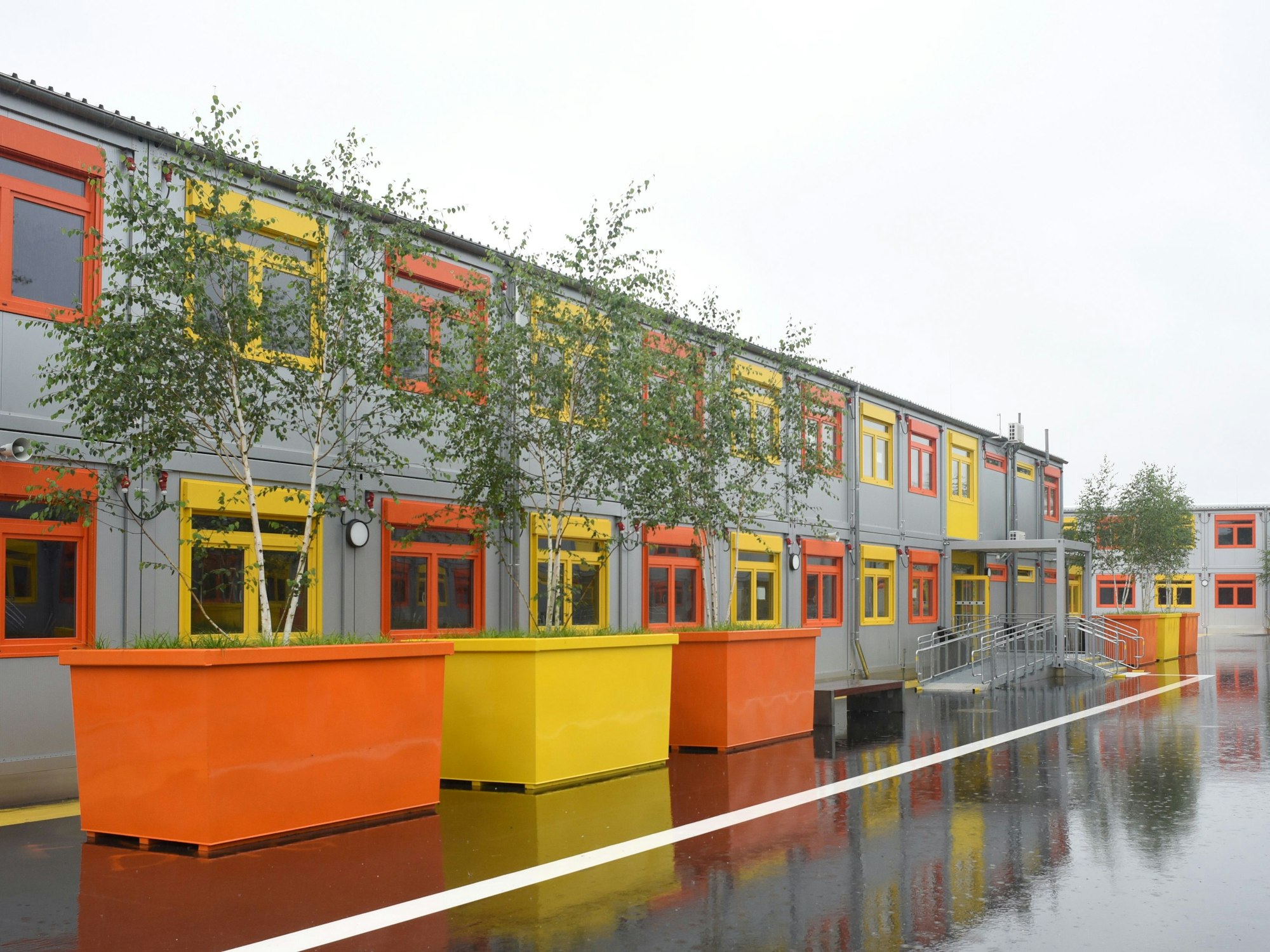 Container-Bauten mit orangefarbenen und gelben Fenstern, davor wurden Bäume in große Kästen gepflanzt.