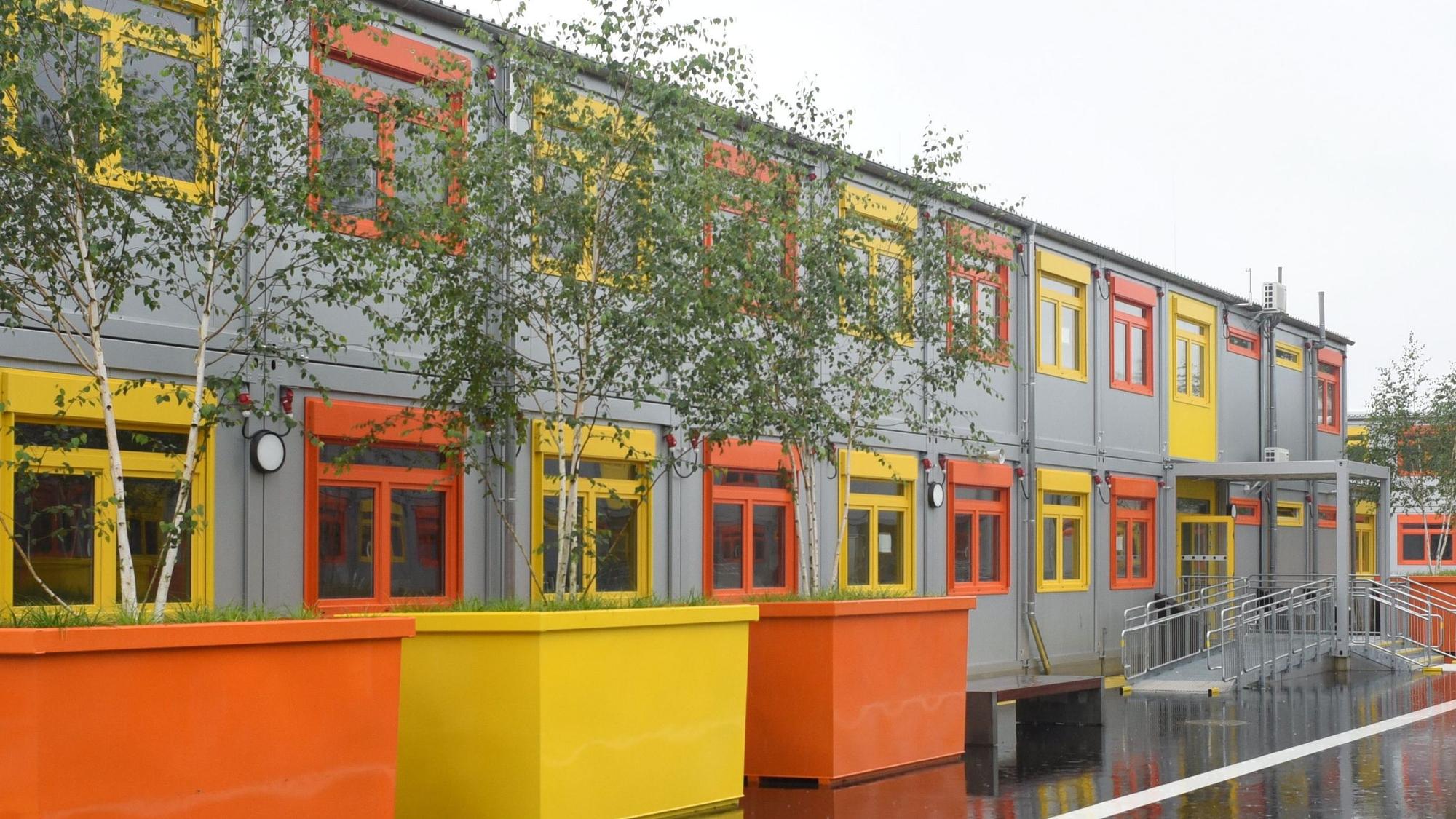 Containerbauten mit orangen und gelben Fenstern und bunten Pflanzkübeln.