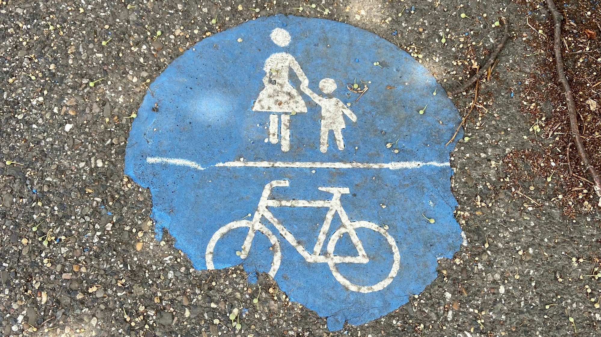 Das Foto zeigt ein Piktogramm auf einem kombinierten Rad- und Fußgängerweg. Die blaue Farbe ist abgesplittert: Ein Sinnbild für die unzureichende Fahrradinfrastruktur im Rhein-Erft-Kreis.