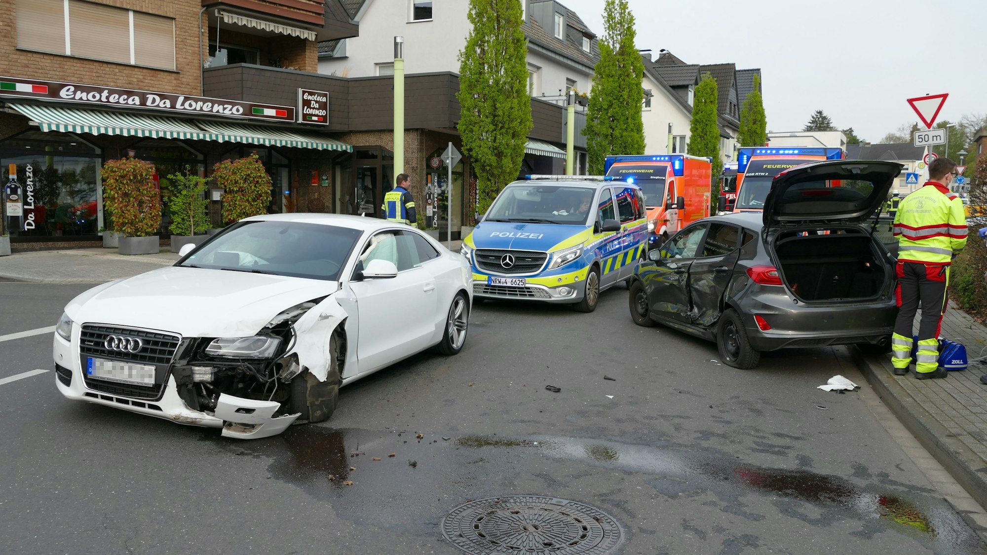 Zwei kaputte Autos stehen auf der Ecke Altenrather Straße/Kirchstraße in Lohmar nach einem Unfall. Feuerwehr und Polizei dazwischen.