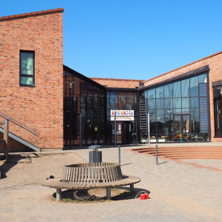 Blick auf den Eingang der Grundschule am Buschweg. Der Himmel ist strahlend blau.