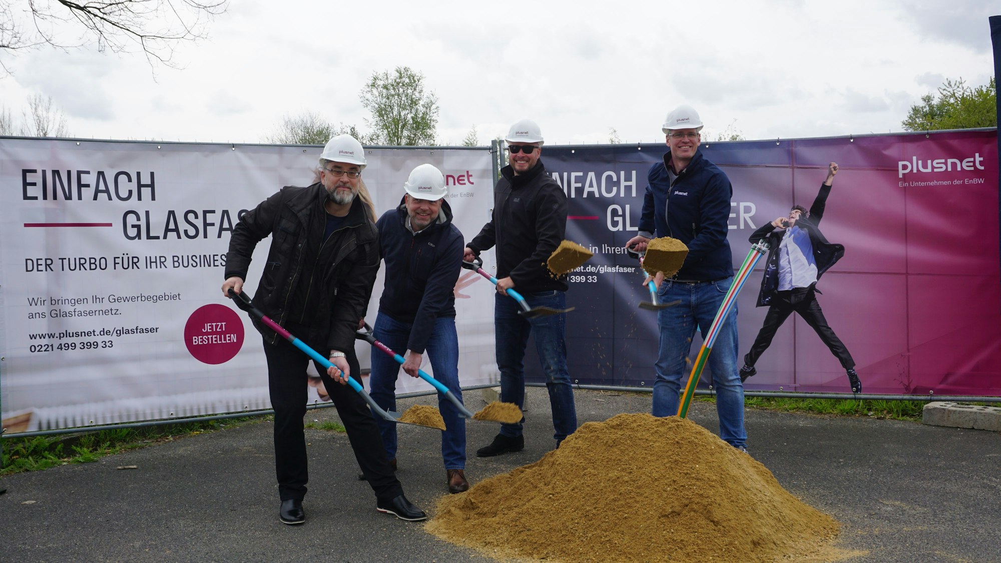 Die Vertreter von Plusnet schaufeln vor Info-Bannern symbolisch Sand.
