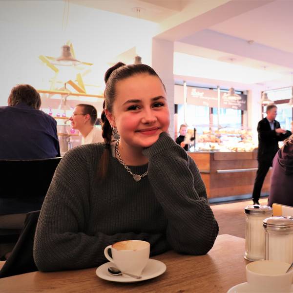 Influencerin Florentine alias „Flobroo“ aus Köln sitzt in einem Lokal, sie trägt einen geflochtenen, dunkelbraunen Pferdeschwanz und eine silberne Gliederkette.