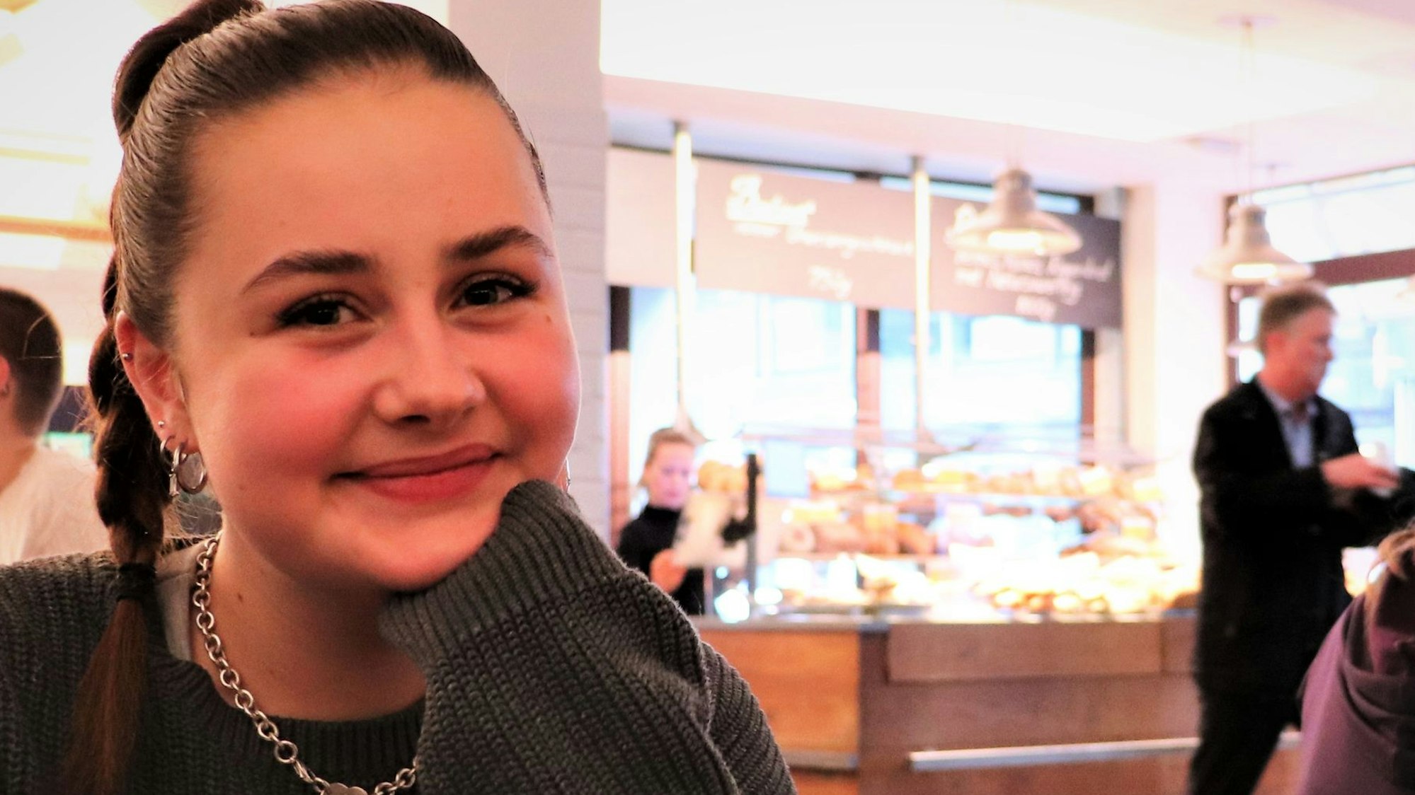 Influencerin Florentine alias „Flobroo“ aus Köln sitzt in einem Lokal, sie trägt einen geflochtenen, dunkelbraunen Pferdeschwanz und eine silberne Gliederkette.