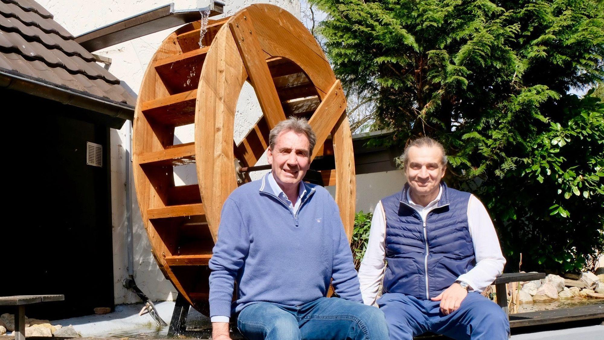 Die beiden sitzen auf einer Mauer vor dem Mühlrad.