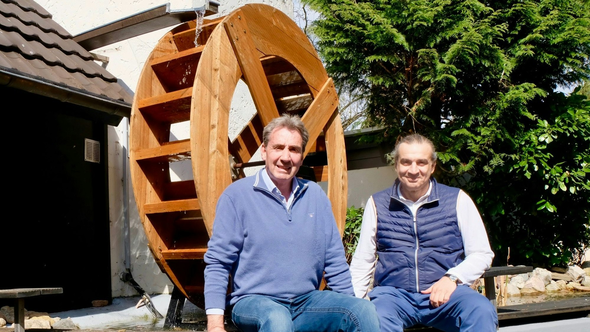 Die beiden sitzen auf einer Mauer vor dem Mühlrad.