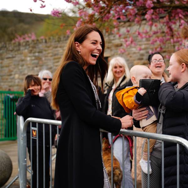 Kate Middleton lacht, während ein Baby mit ihrer Handtasche spielt. Seine Mutter hält das Baby auf dem Arm.