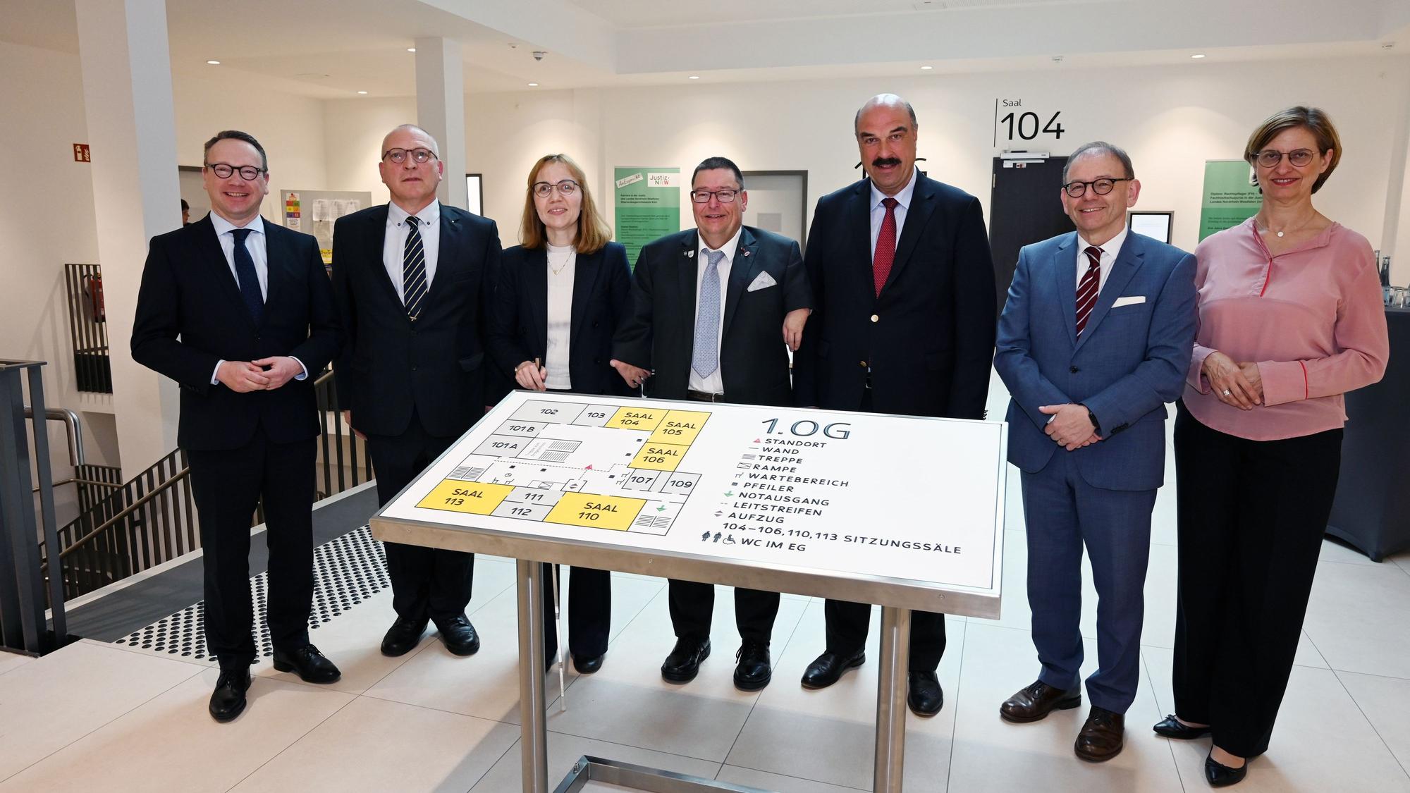 Mehrere Männer und Frauen stehen in einem Gerichtsgebäude vor einer großen Tafel für Sehbehinderte.
