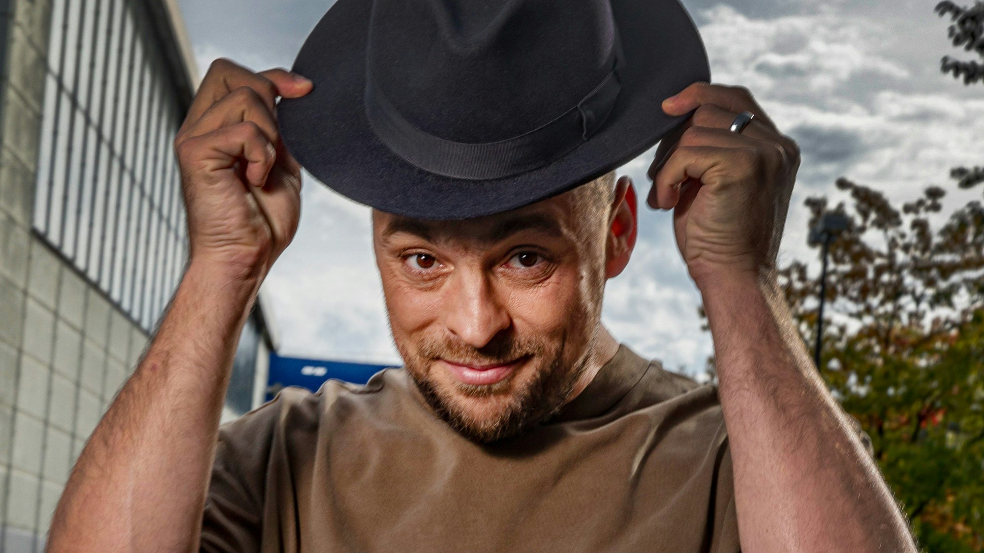 Sänger Max Mutzke lächelt in die Kamera und hebt seinen Hut an.