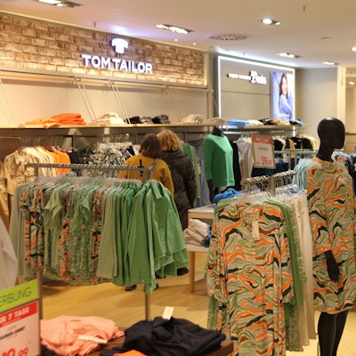 Auf Kleiderständern hängen Kleider und Blusen, im Hintergrund ist eine Kundin.