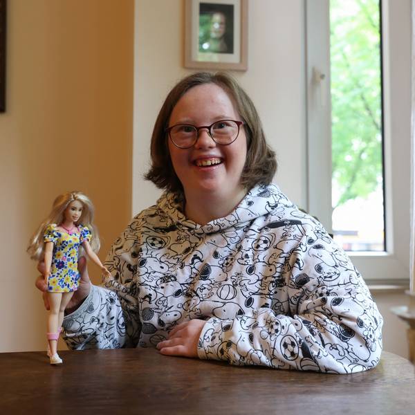 Die Kölnerin Natalie Dedreux lacht in die Kamera und hält die neue Barbie mit Down-Syndrom in ihrer rechten Hand.