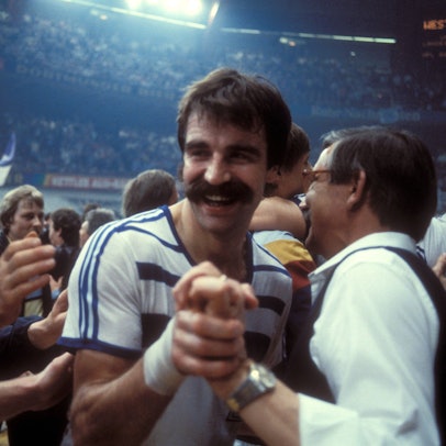 Im Bild ist ein Menschenauflauf zu sehen, die Personen freuen sich und gratulieren einander. Mittendrin ist Handball-Legende Heiner Brand.