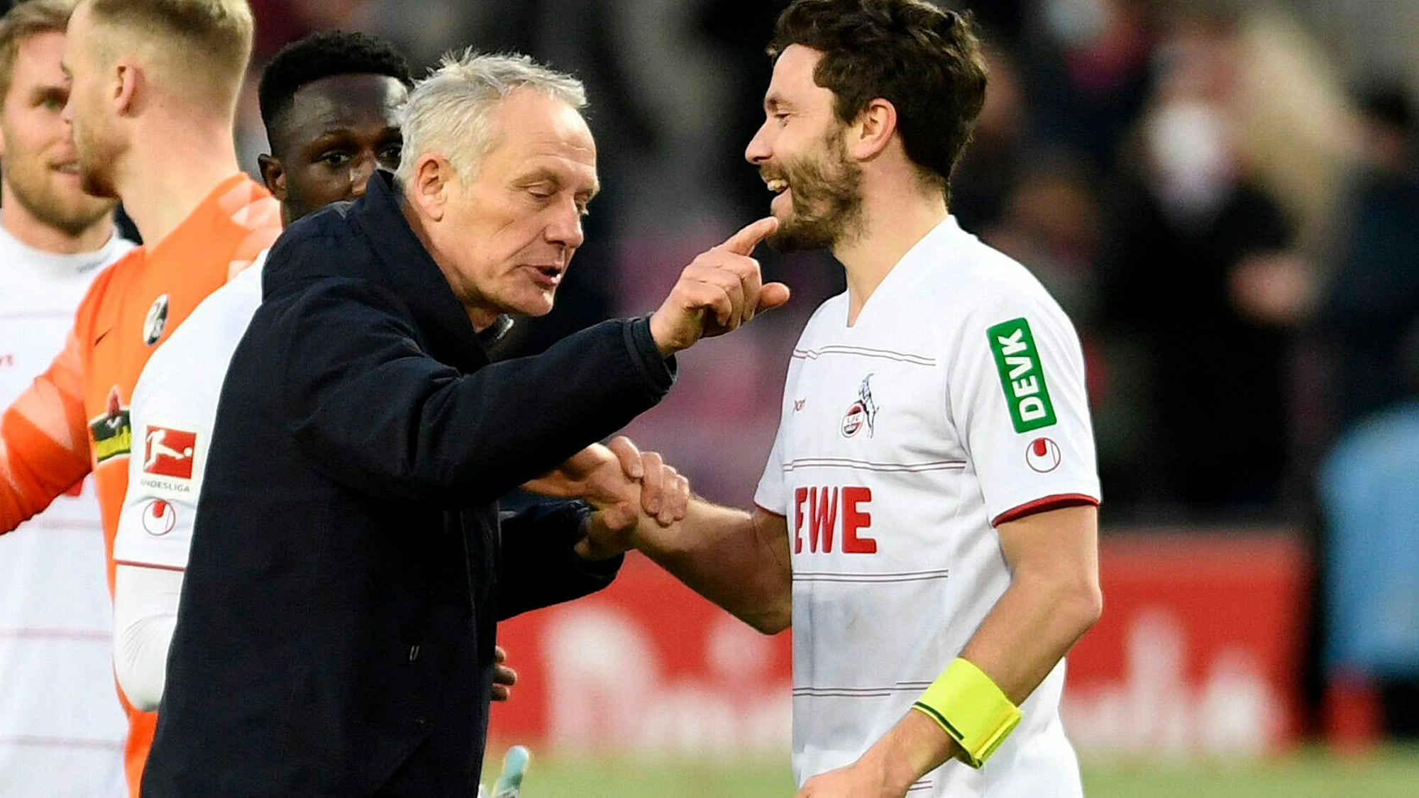 Freiburgs Trainer Christian Streich gestikuliert nach dem Spiel zwischen Freiburg und Köln im Rhein-Energie-Stadion, Jonas Hector hört lächelnd zu.