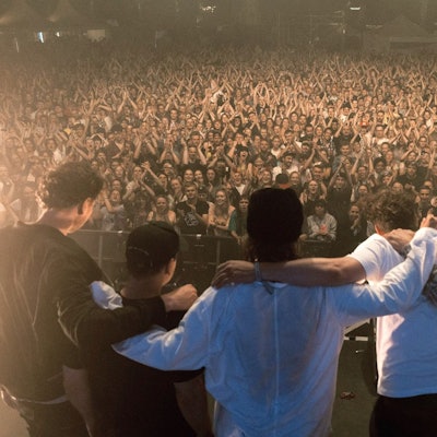 Die Band steht Arm in Arm vor ihren Zuschauern und Zuschauerinnen auf der Bühne.