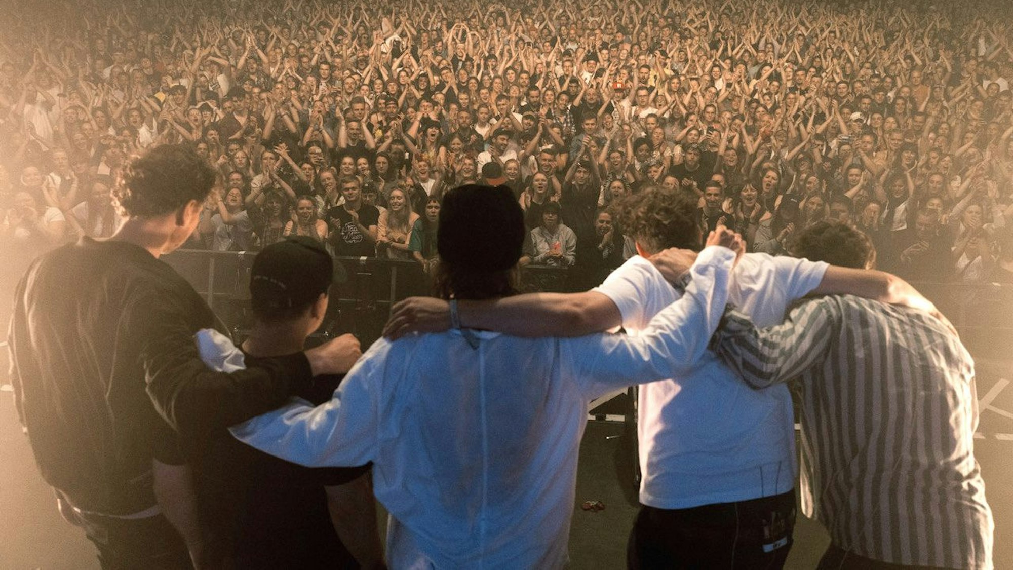 Die Band steht Arm in Arm vor ihren Zuschauern und Zuschauerinnen auf der Bühne.