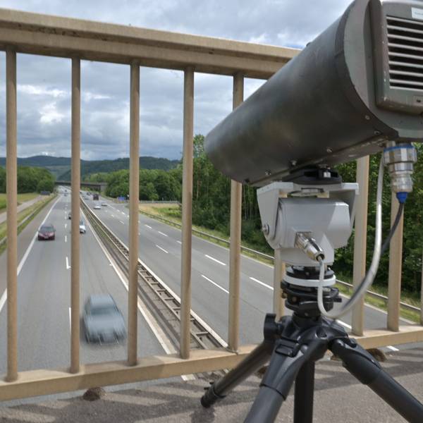 Eine Monocam zur Aufzeichnung von Handysündern am Steuer steht auf einer Brücke über einer Autobahn.