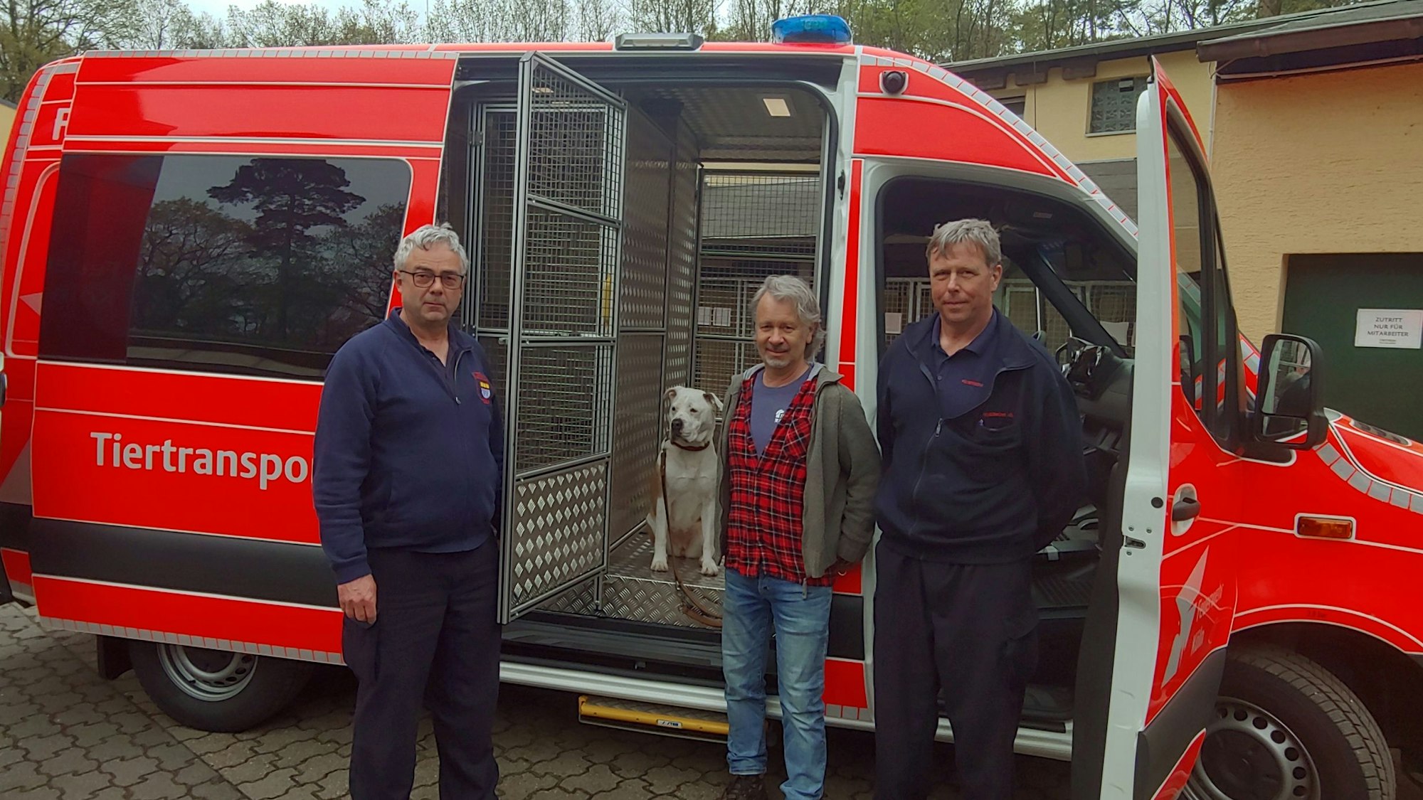 Josef Nehler (l.) und Hubert Hennig (r.) von der Kölner Feuerwehr stehen vor dem roten Einsatzfahrzeug. In der Mitte steht der Leiter des Tierheims Dellbrück, Bernd Schinzel mit Hündin Kira.
