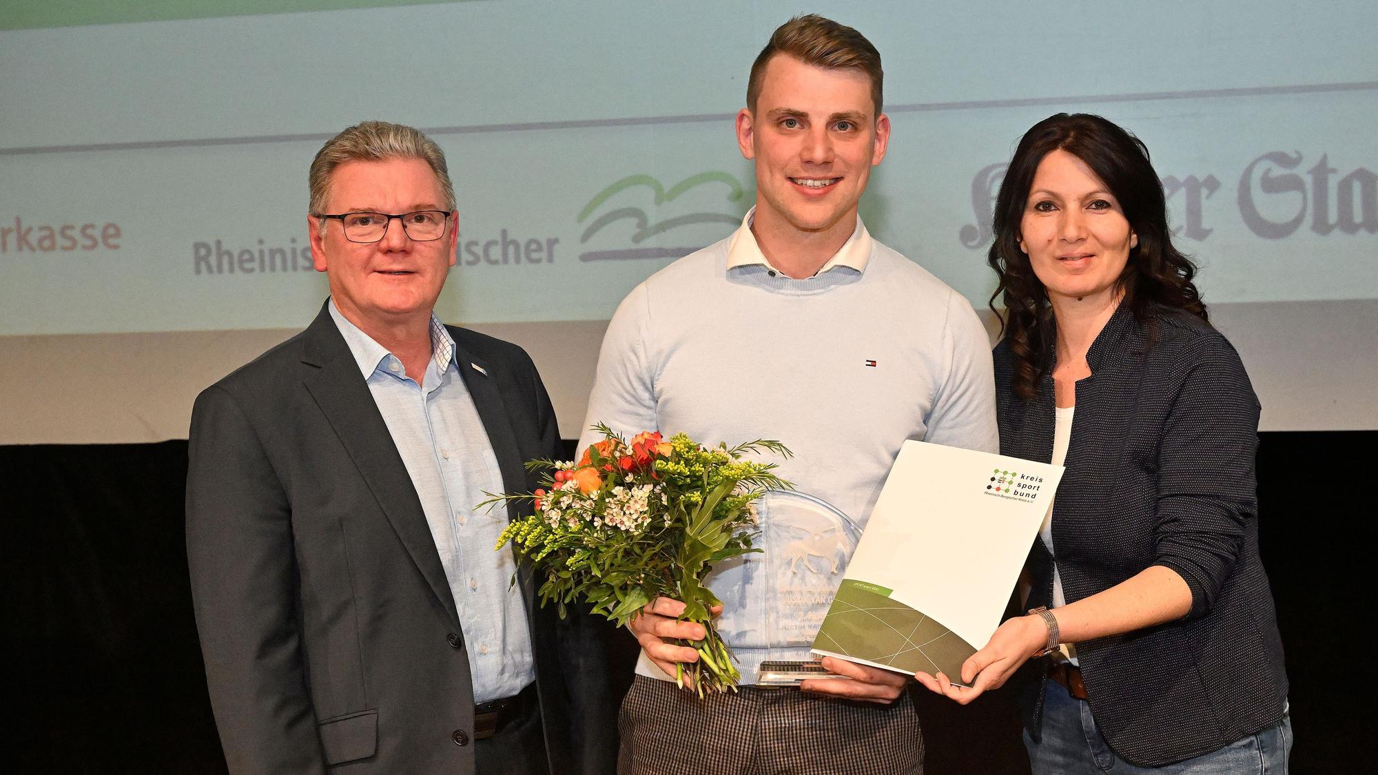 Drei Menschen stehen mit Blumen und Sportlerehrungsurkunge auf einer Bühne.