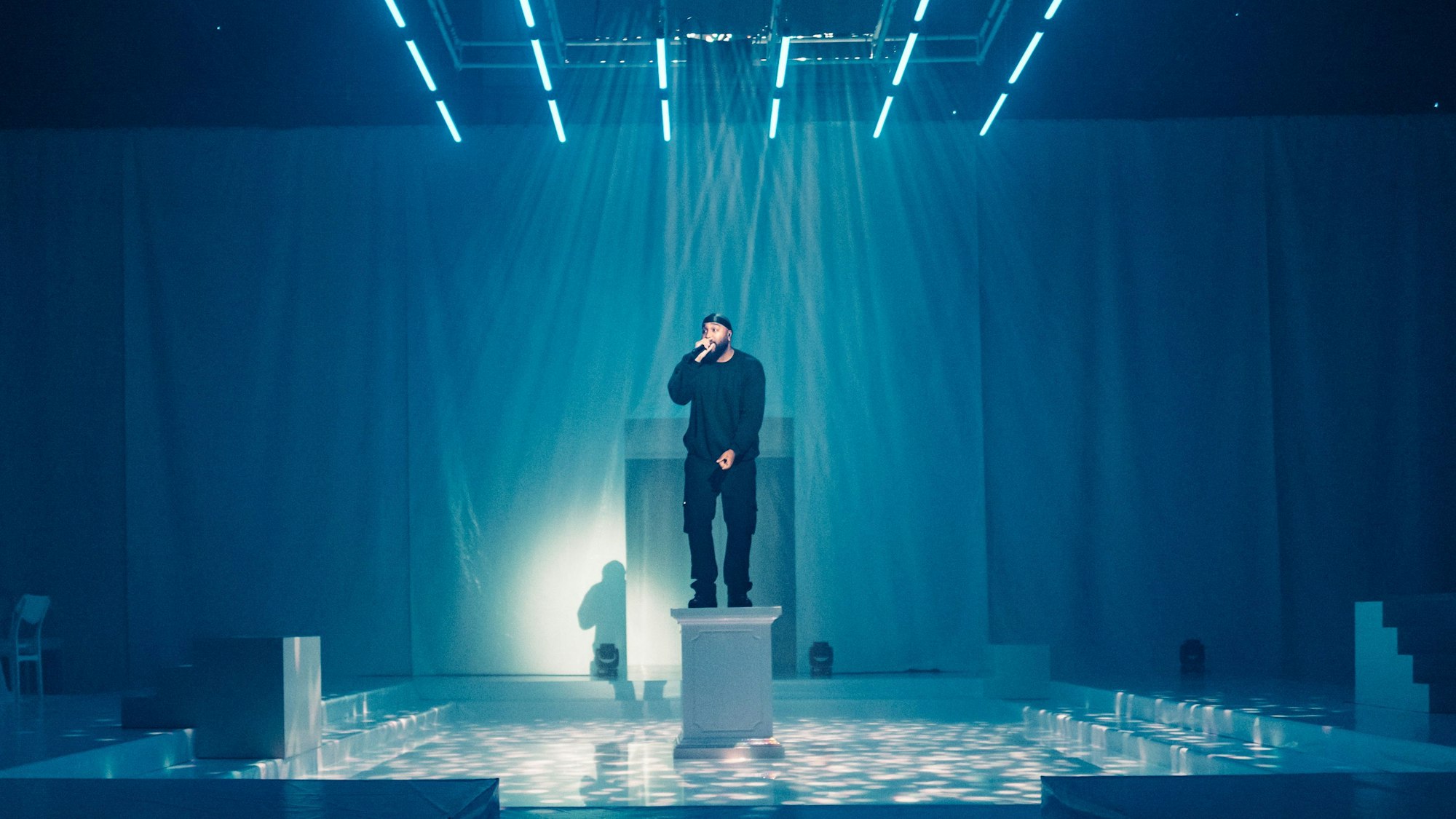 Rapper OG Keemo steht auf einer weißen Säule im Bühnenbild von "Die Troerinnen" im Depot 1 des Schauspiels Köln.